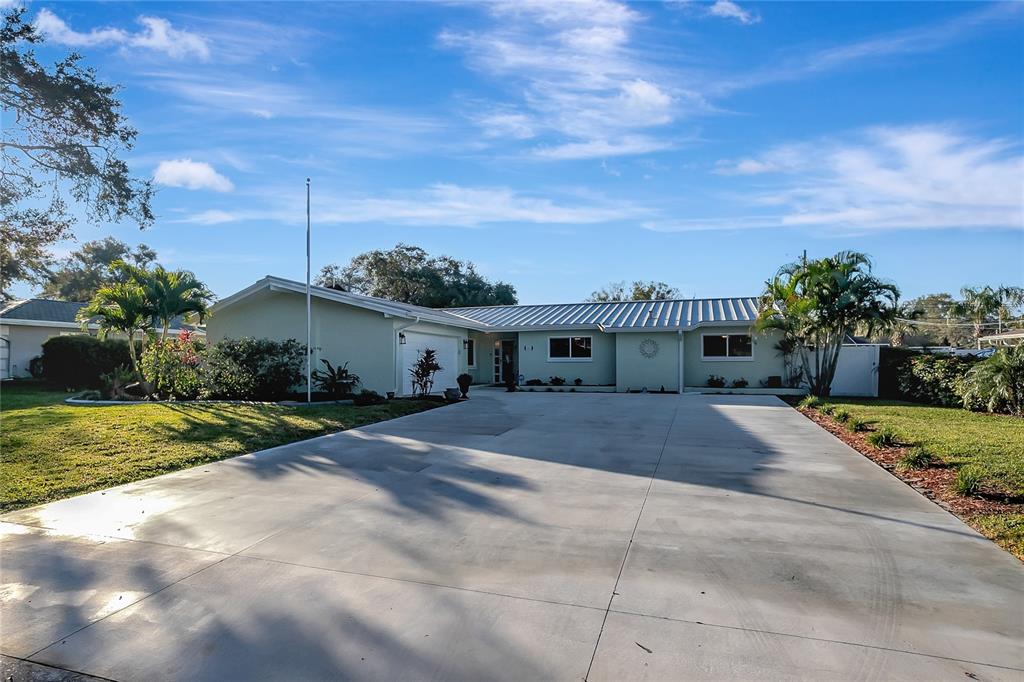 A single-story house with a metal roof and a large concrete driveway under a sky — 809 JACARANDA DRIVE, LARGO, FL