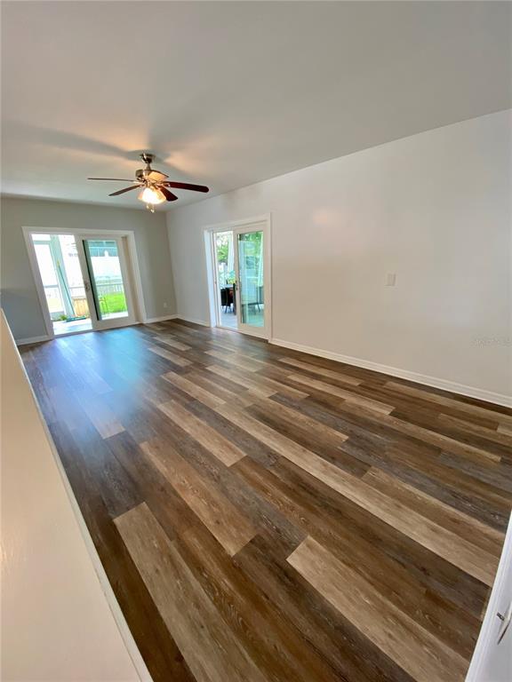 An empty room features wood-look flooring, a ceiling fan, and two sets of sliding glass doors — 809 JACARANDA DRIVE, LARGO, FL