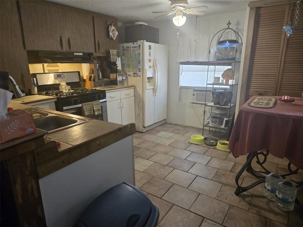 A kitchen with brown cabinets, tile flooring, a white refrigerator, and a small dining table — 120 WEST LOOP, OAK HILL, FL