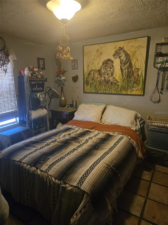 A bedroom features a bed with a patterned blanket, a large lion painting, and tile flooring — 120 WEST LOOP, OAK HILL, FL