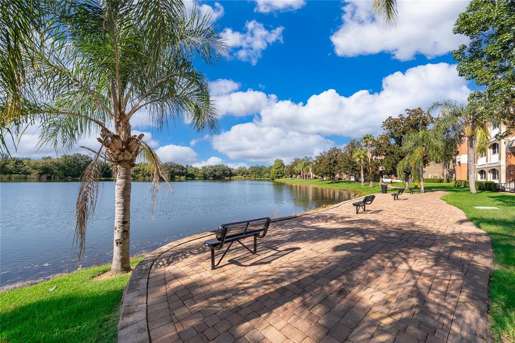 A brick walkway with benches runs alongside a lake near a palm tree and apartments — 1939 SUMMER CLUB DRIVE UNIT 115, OVIEDO, FL