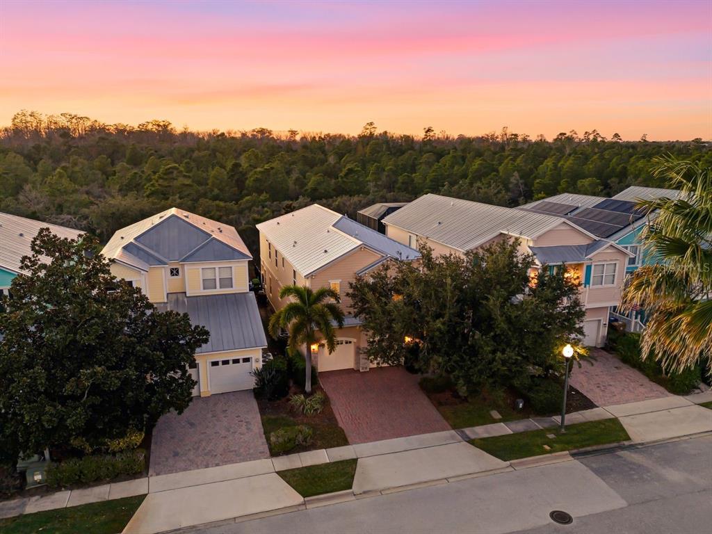 An aerial view shows three suburban houses with metal roofs and paved driveways at sunset — 1437 FAIRVIEW CIRCLE, REUNION, FL