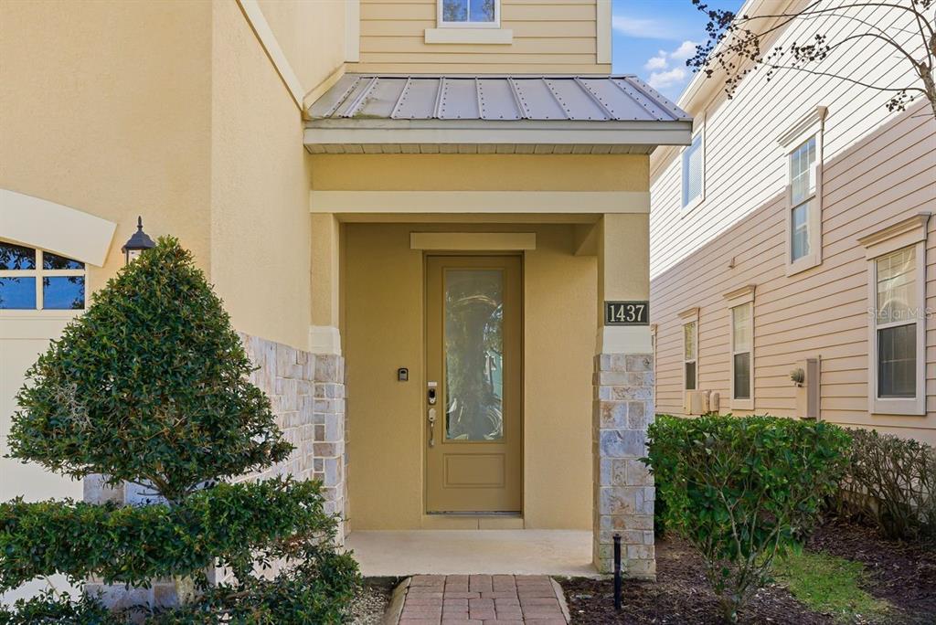 The front entrance of a house features a tan door, stone pillars, and a metal roof — 1437 FAIRVIEW CIRCLE, REUNION, FL