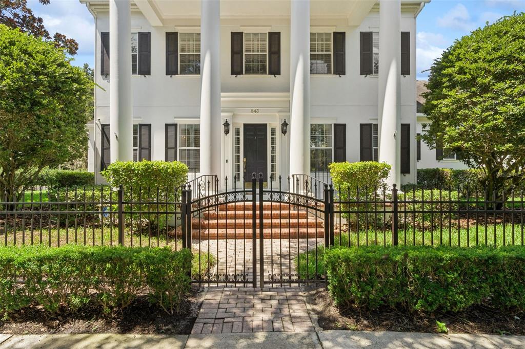 A two-story white house with a columned portico stands behind a manicured hedge and fence — 843 OAK SHADOWS ROAD, CELEBRATION, FL