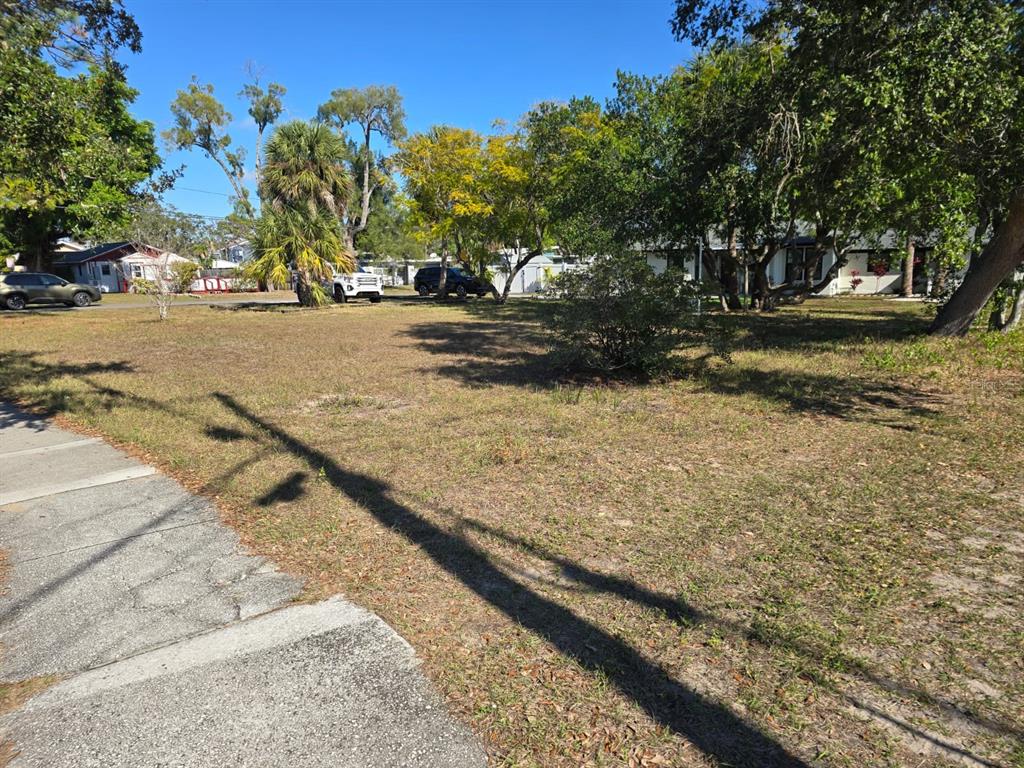 A vacant, grassy residential lot features several mature trees and a sidewalk in the foreground — MILWAUKEE AVENUE, DUNEDIN, FL