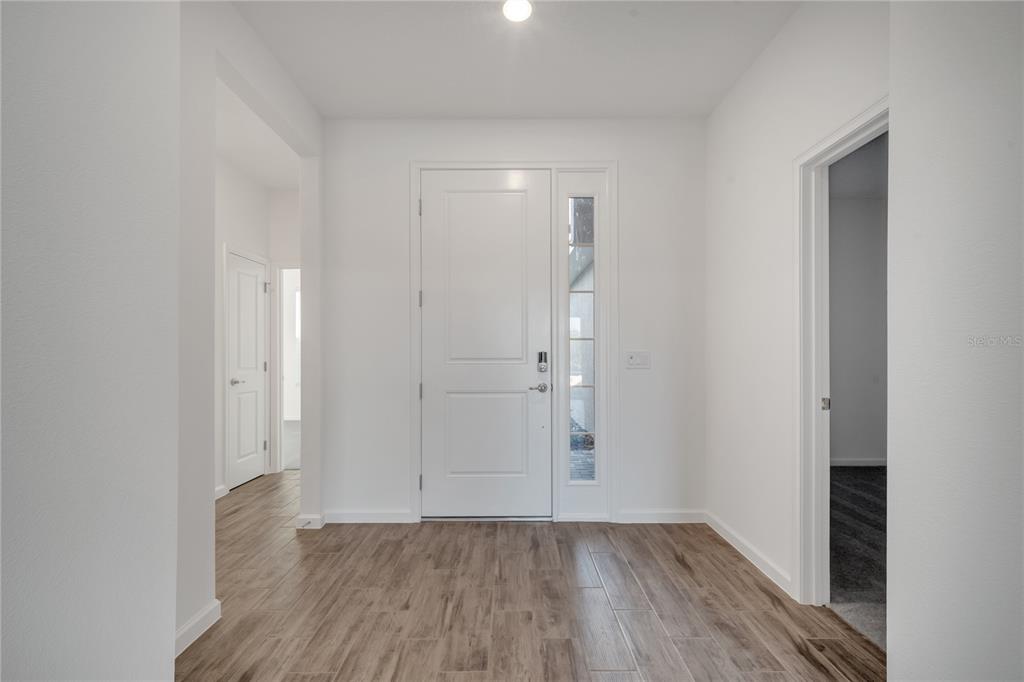 An entryway features white walls, a front door with a sidelight, and wood-look tile flooring — 2272 SIRENS LANE, MOUNT DORA, FL