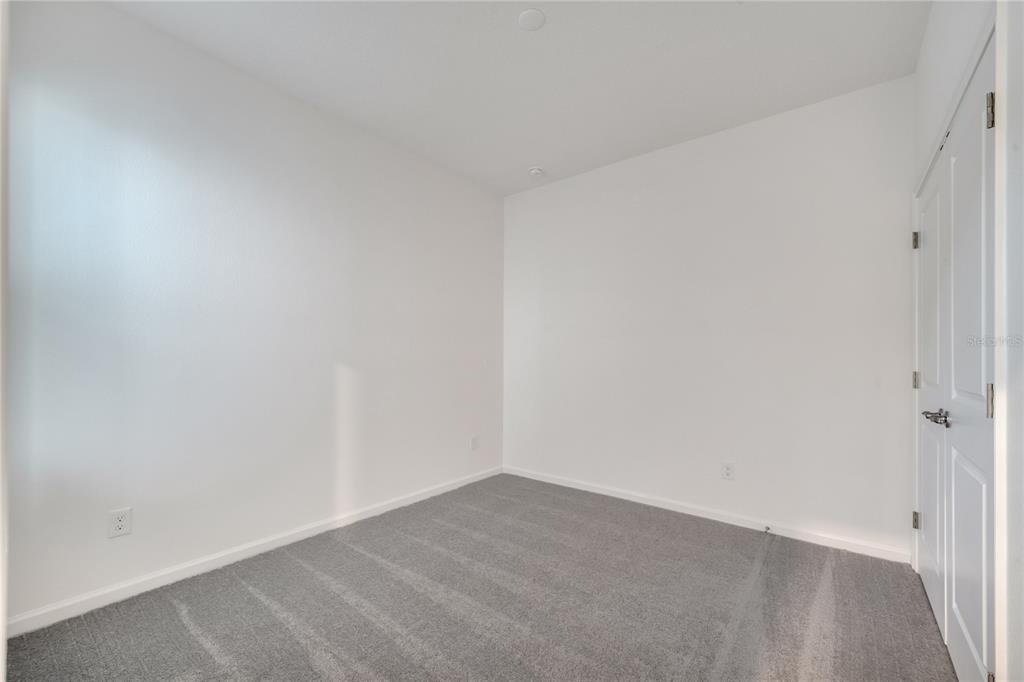 An empty room with white walls, gray carpet, and a white door on the right — 2272 SIRENS LANE, MOUNT DORA, FL