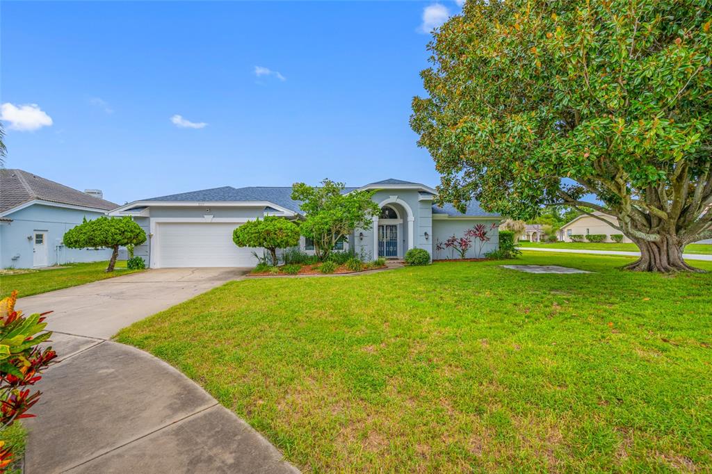 A single-story house with a white garage, arched entryway, and a large tree in front — 3225 HEARTHSTONE COURT, HOLIDAY, FL