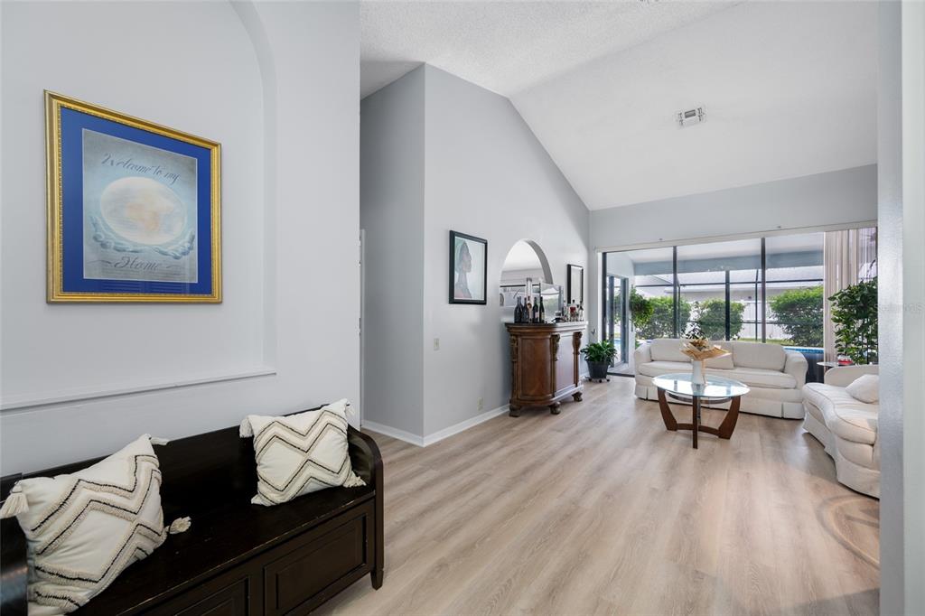 A bright living room features light wood flooring, vaulted ceilings, and a large sliding glass door — 3225 HEARTHSTONE COURT, HOLIDAY, FL