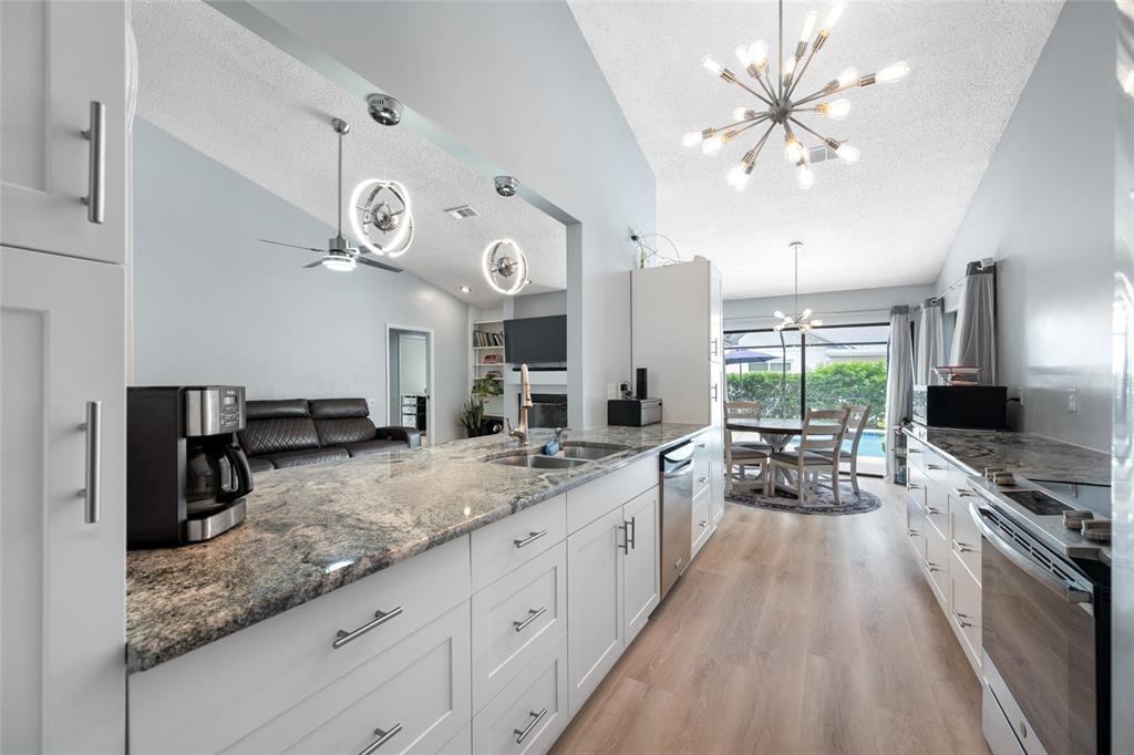 A modern kitchen features white cabinetry, granite countertops, and a view into the living area — 3225 HEARTHSTONE COURT, HOLIDAY, FL