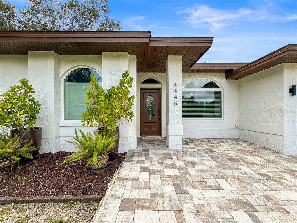 The exterior of a house features a paved walkway, a brown front door, and arched windows — 4448 GLENBROOK DRIVE, PALM HARBOR, FL