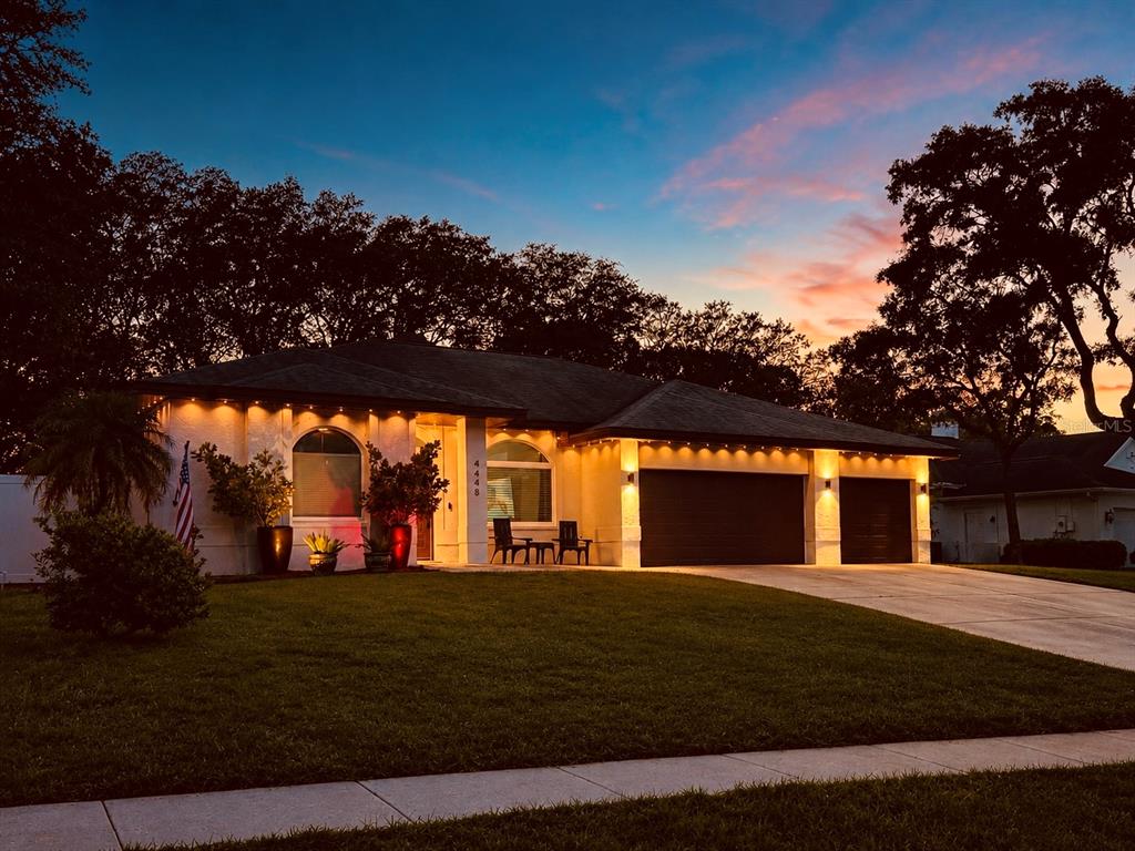 A single-story house with a two-car garage and exterior lighting at dusk — 4448 GLENBROOK DRIVE, PALM HARBOR, FL