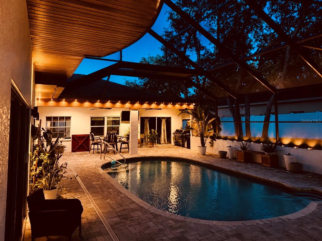 An illuminated swimming pool sits on a paved patio beneath a screened-in lanai at dusk — 4448 GLENBROOK DRIVE, PALM HARBOR, FL