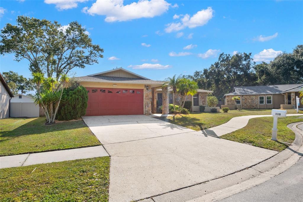 A single-story house with a red garage door, stone accents, and a concrete driveway — 110 MEADOWCROSS DRIVE, SAFETY HARBOR, FL