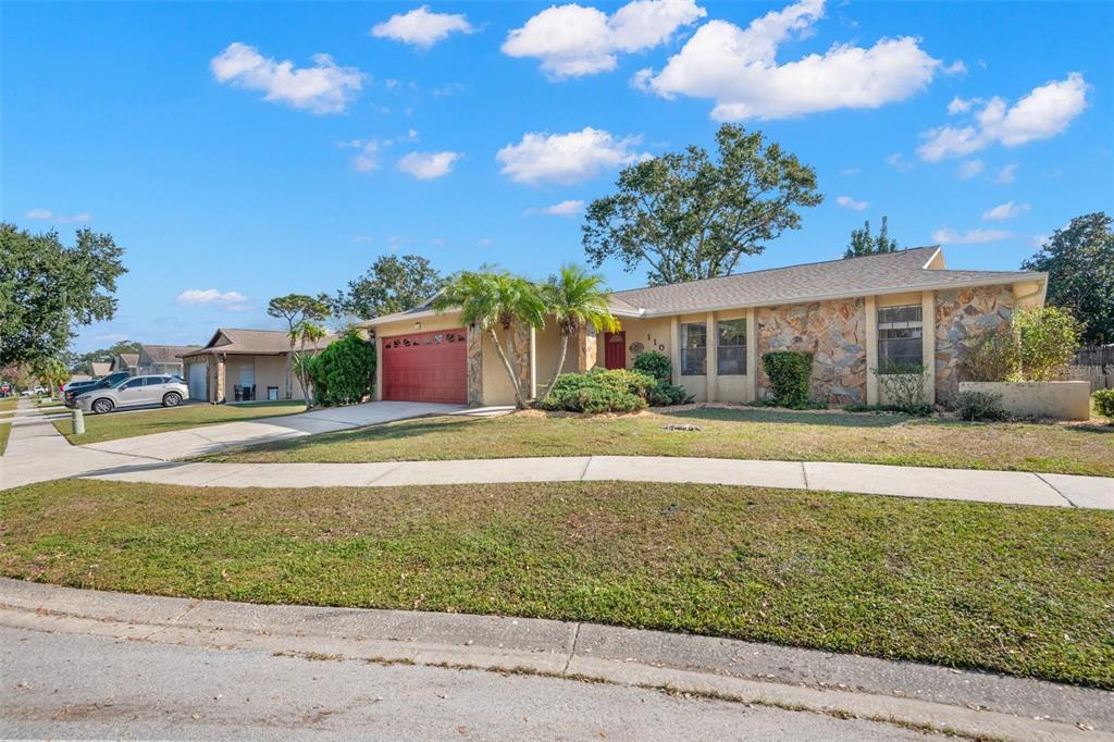 A single-story house with a stone facade, red garage door, and palm trees in front — 110 MEADOWCROSS DRIVE, SAFETY HARBOR, FL