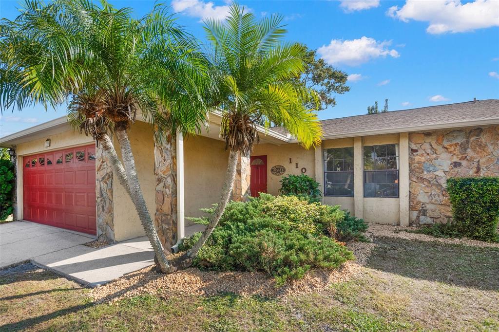 A single-story house features a red garage door, stone accents, and two palm trees — 110 MEADOWCROSS DRIVE, SAFETY HARBOR, FL