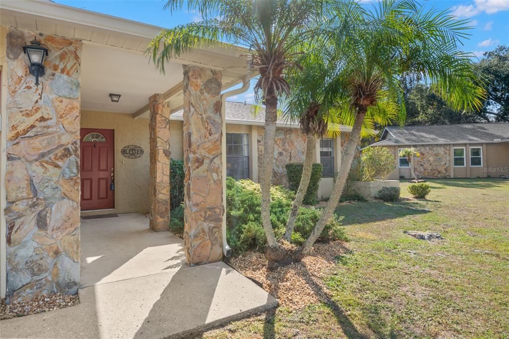 A stone-faced house exterior features a covered entryway with a red door and palm trees — 110 MEADOWCROSS DRIVE, SAFETY HARBOR, FL