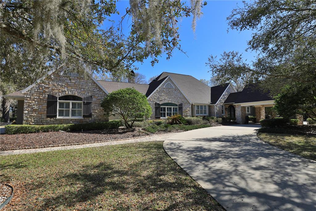 A stone-clad house with a curved concrete driveway and a covered entryway under trees — 7963 SE 12TH CIRCLE, OCALA, FL