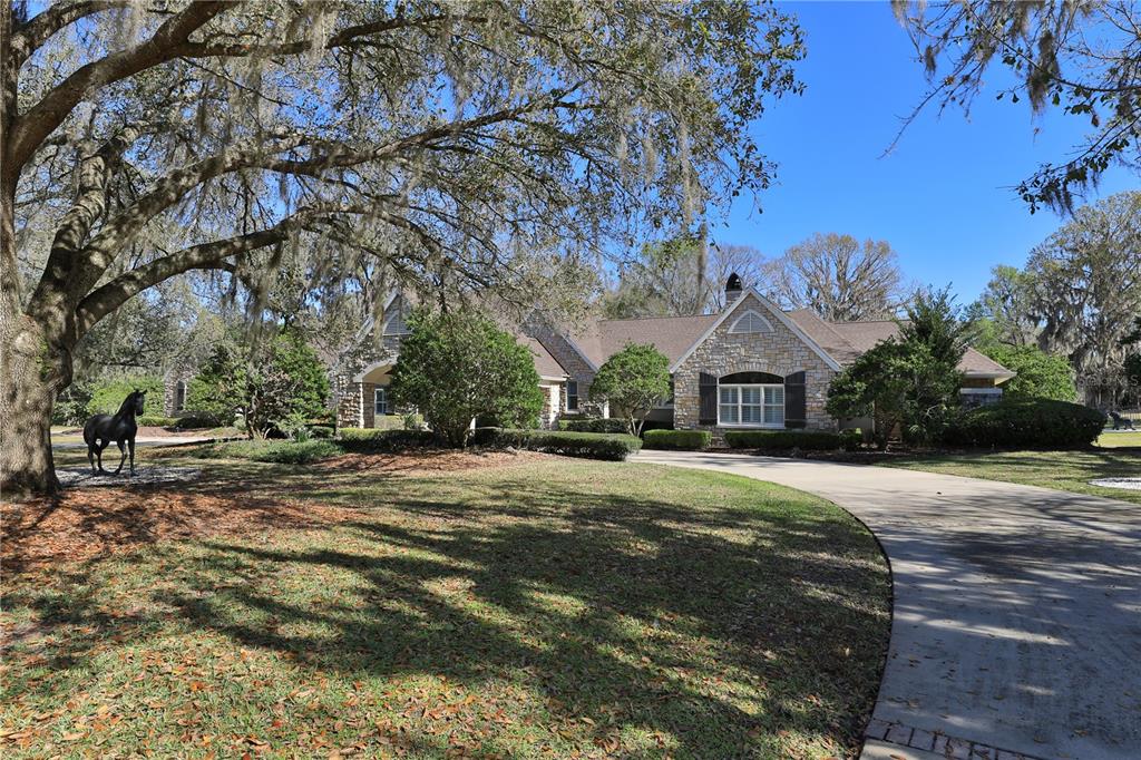 A stone-faced house with a curved driveway and a horse statue on the lawn — 7963 SE 12TH CIRCLE, OCALA, FL