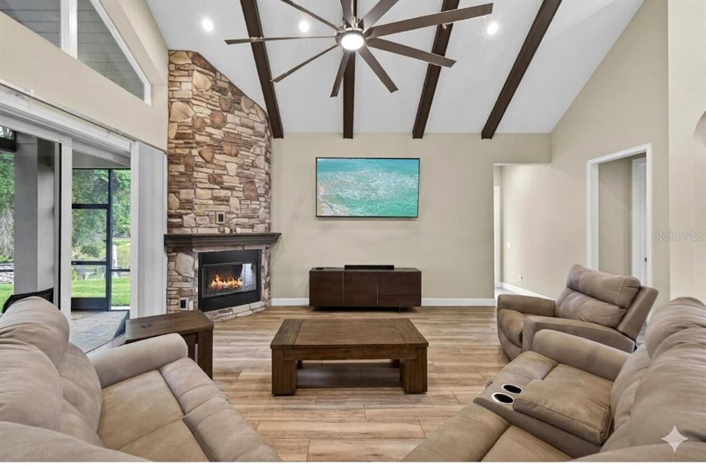 A living room features a stone fireplace, vaulted ceilings with exposed beams, and wood-look flooring — 1208 SUNSET LANE, LUTZ, FL