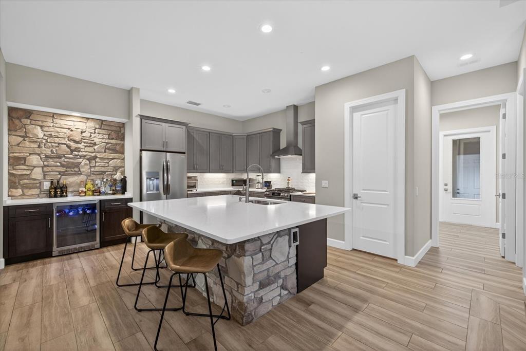A kitchen features a stone-accented island, gray cabinetry, quartz countertops, and wood-look tile flooring — 1208 SUNSET LANE, LUTZ, FL