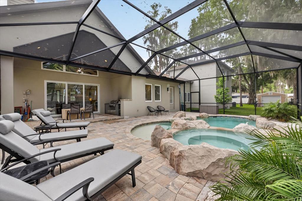 A screened-in patio features a stone-accented pool and spa with lounge chairs on pavers — 1208 SUNSET LANE, LUTZ, FL