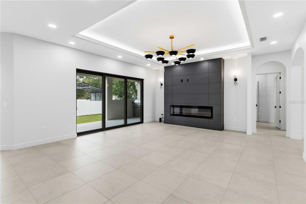 A modern living room features large tile floors, a dark fireplace wall, and sliding glass doors — 104 S MAKI ROAD, PLANT CITY, FL
