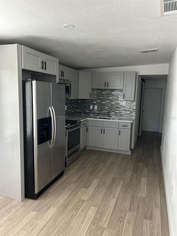 A kitchen features gray cabinets, stainless steel appliances, and a tiled backsplash — 73 BROOKS DRIVE, ORMOND BEACH, FL