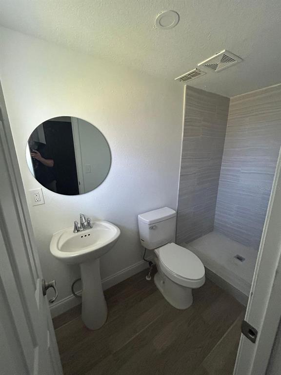 A bathroom features a pedestal sink, a round mirror, a toilet, and a tiled shower — 73 BROOKS DRIVE, ORMOND BEACH, FL
