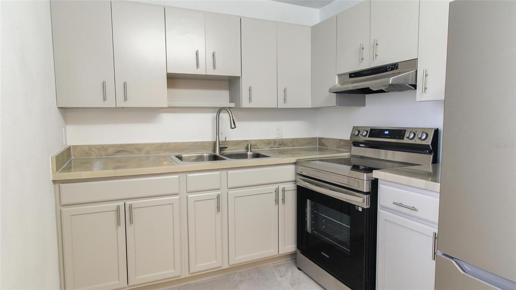 A kitchen features light gray cabinets, stainless steel appliances, and a tan laminate countertop — 2509 OAK PARK WAY UNIT 115, ORLANDO, FL