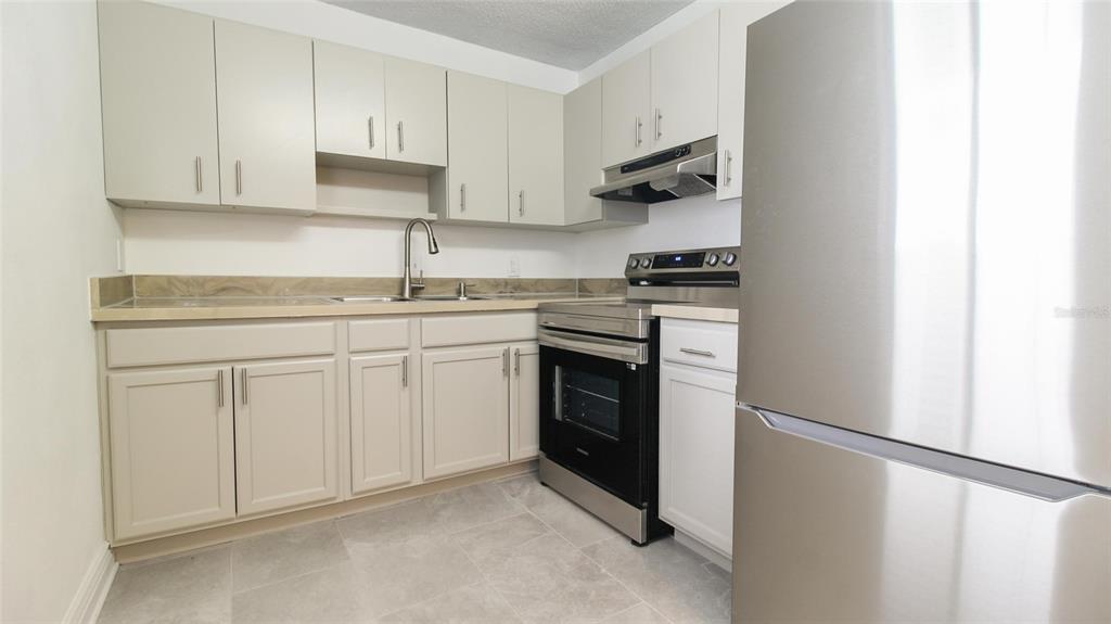A kitchen features light-colored cabinets, stainless steel appliances, and a tiled floor — 2509 OAK PARK WAY UNIT 115, ORLANDO, FL