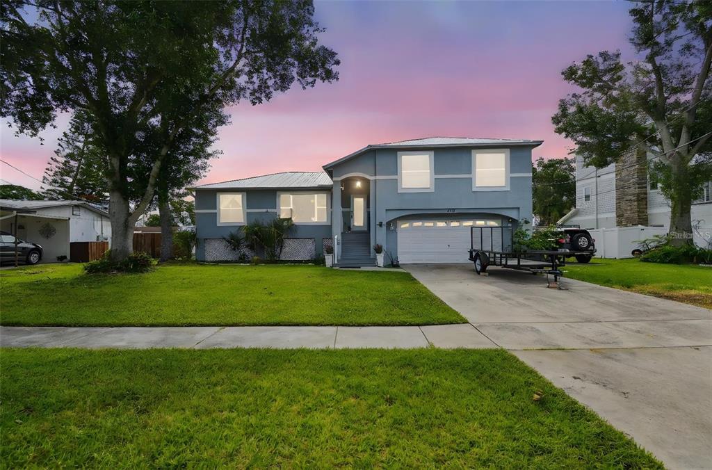 A two-story blue house with a white garage door and a front lawn at dusk — 317 SHORE DRIVE E, OLDSMAR, FL