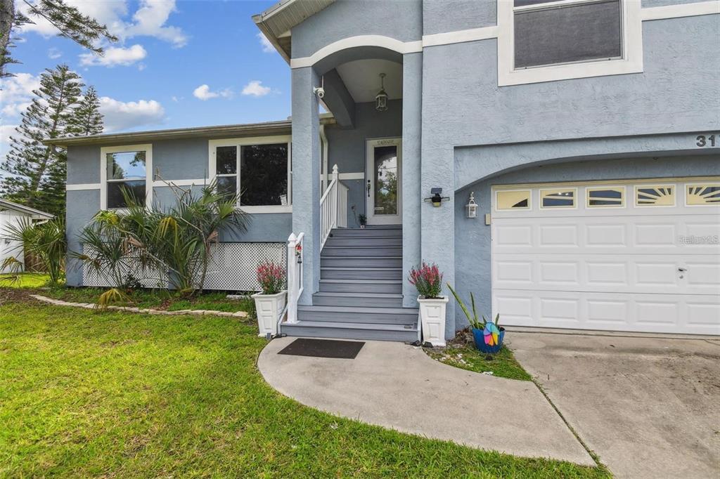 A blue two-story house features a front-facing garage, elevated entryway stairs, and a concrete walkway — 317 SHORE DRIVE E, OLDSMAR, FL