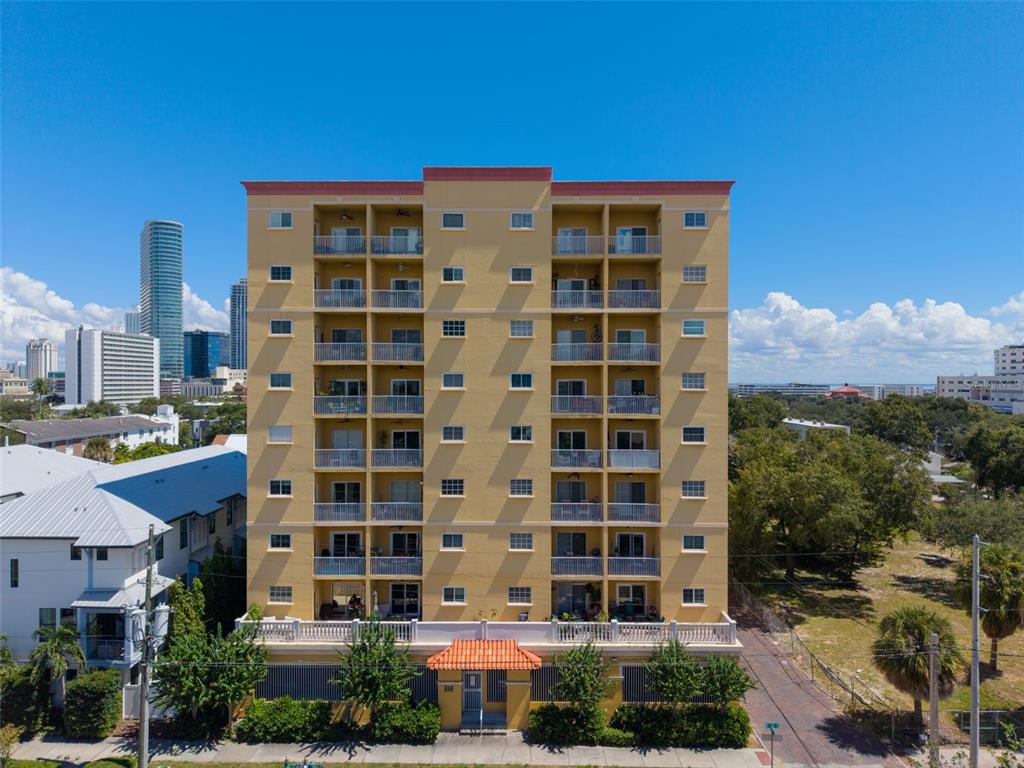 An exterior view of a multi-story yellow apartment building with balconies under a blue sky — 316 8TH STREET S UNIT 703, ST PETERSBURG, FL