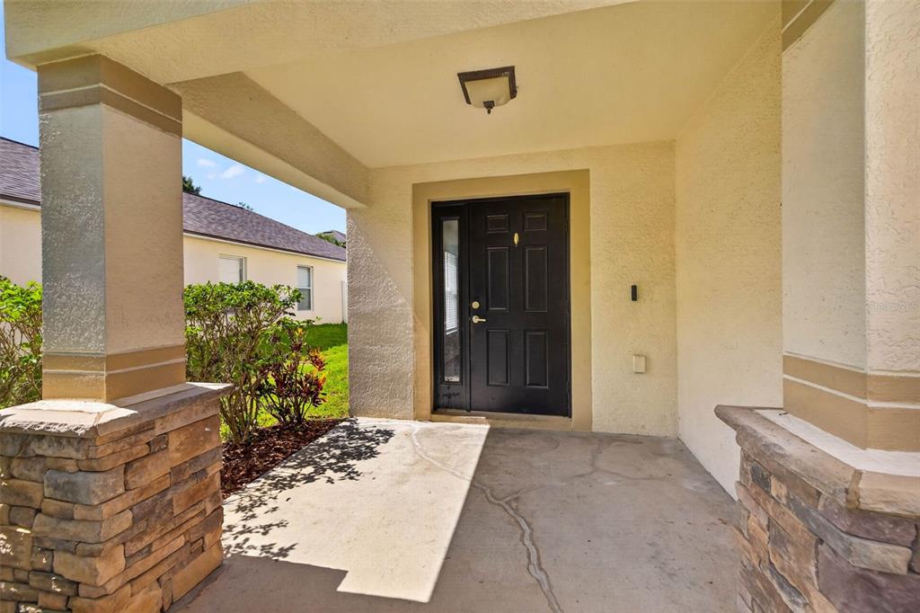 A covered front porch features a black door, stone-accented columns, and a concrete floor — 10717 SHADY PRESERVE DRIVE, RIVERVIEW, FL