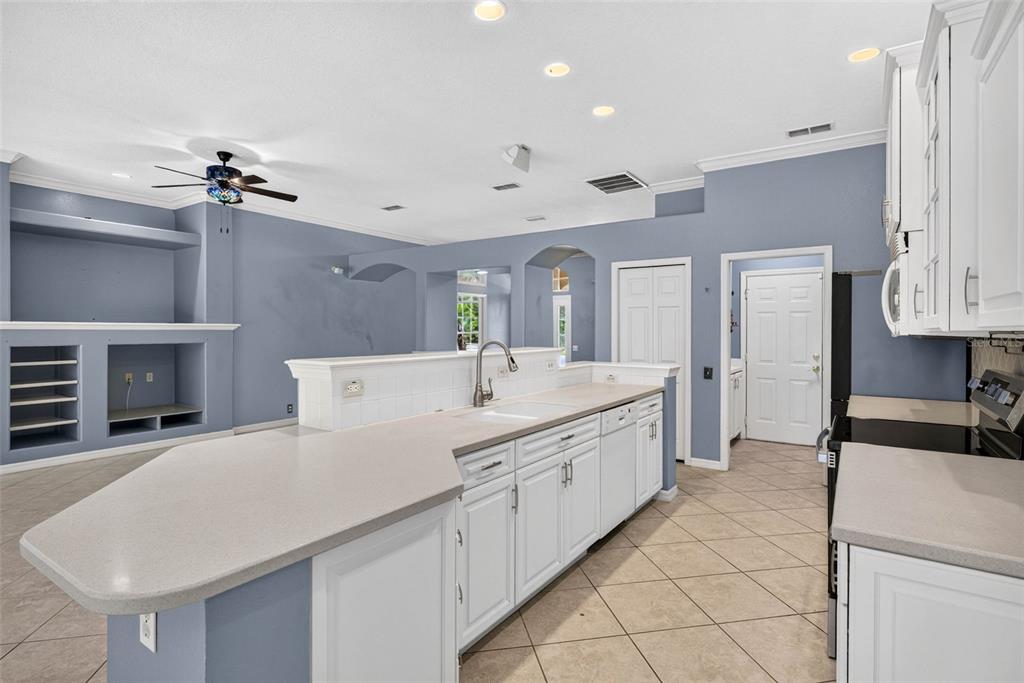 A kitchen with white cabinets and a peninsula overlooks a living area with blue walls — 12 NICOTIANA COURT, HOMOSASSA, FL