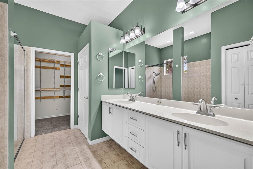 A bathroom with a double vanity, large mirror, green walls, and an adjacent walk-in closet — 12 NICOTIANA COURT, HOMOSASSA, FL