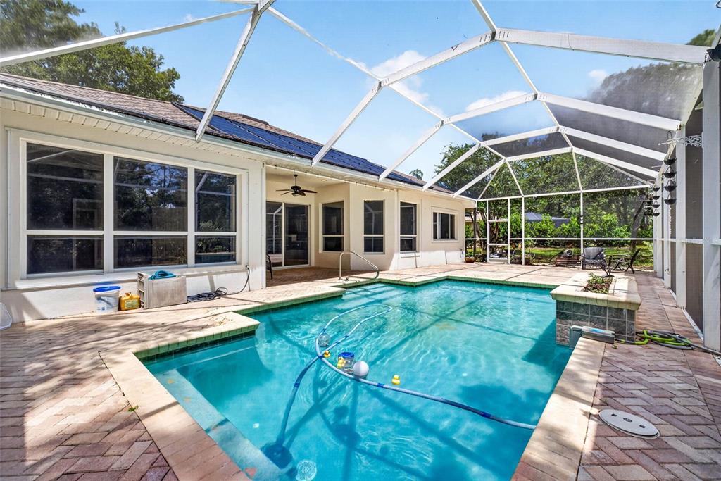 A swimming pool with a screen enclosure sits on a brick patio behind a house — 12 NICOTIANA COURT, HOMOSASSA, FL