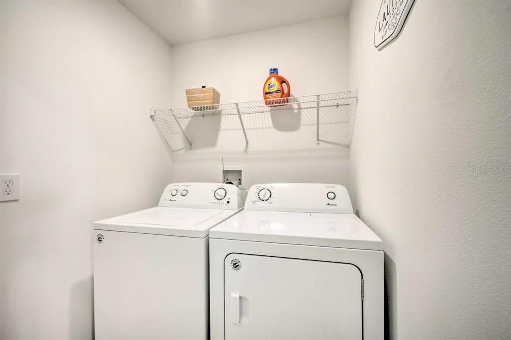 A laundry room features a white washer and dryer beneath a wire storage shelf — 709 BENOI DRIVE, DAVENPORT, FL