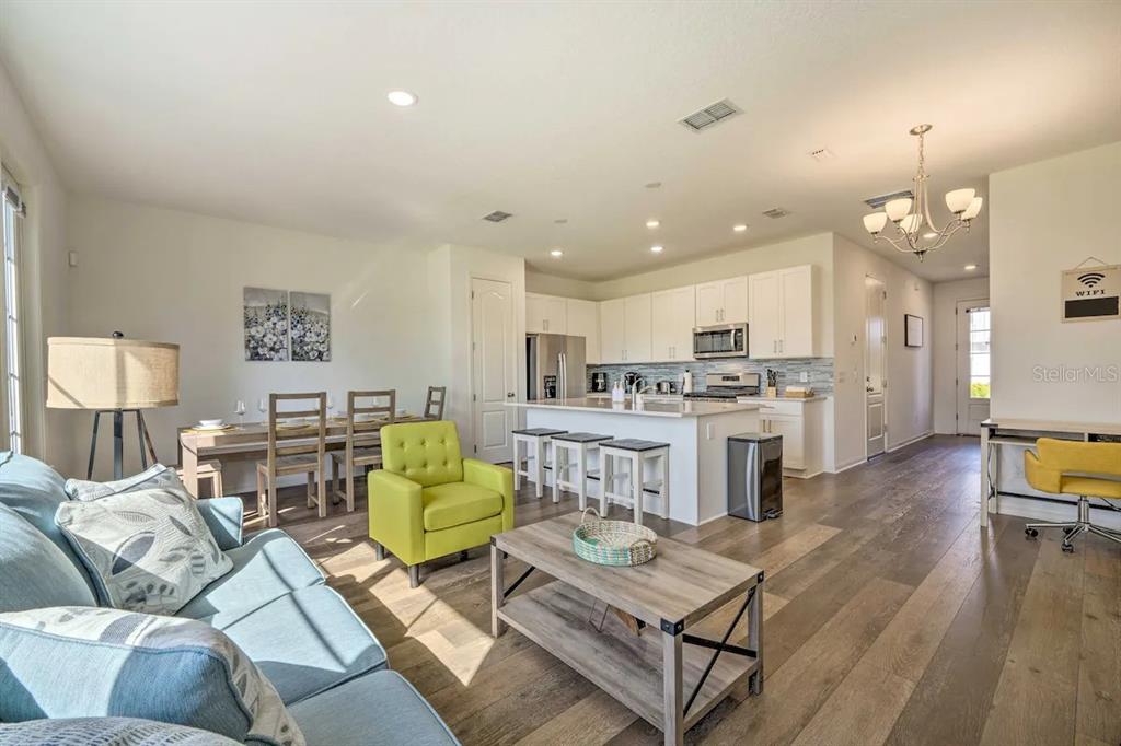 An open-concept living room and kitchen featuring light wood floors, white cabinetry, and modern furniture — 709 BENOI DRIVE, DAVENPORT, FL