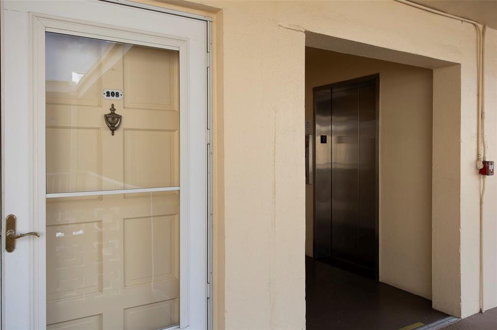 A white door labeled 208 sits next to a stainless steel elevator in a hallway — 1200 N SHORE DRIVE NE UNIT 208, ST PETERSBURG, FL