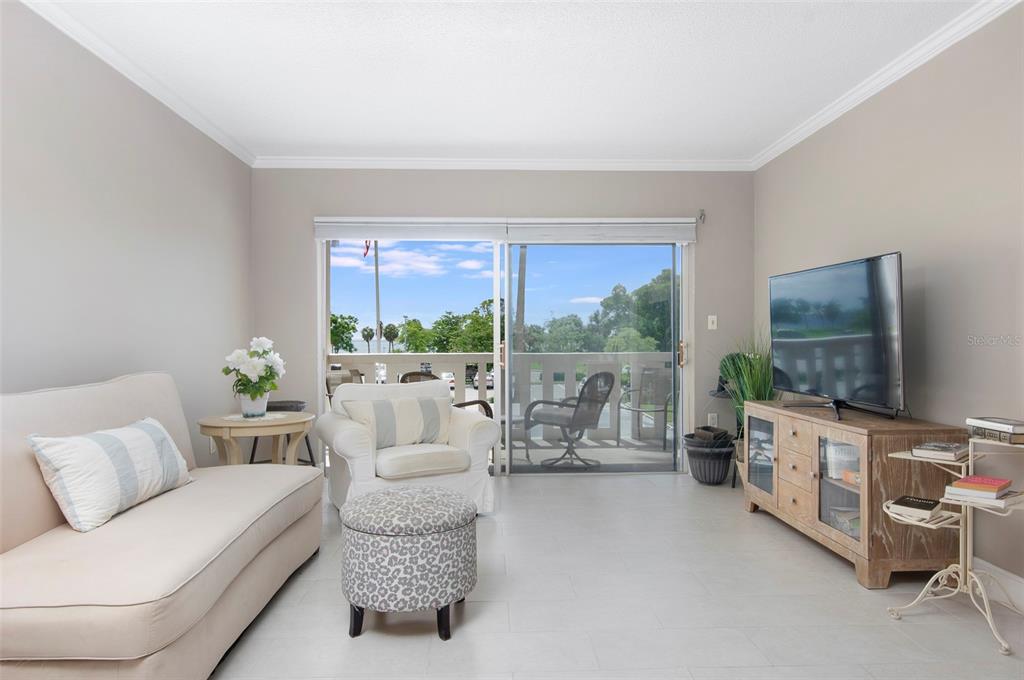 A living room features a beige sofa, armchair, ottoman, television console, and sliding glass balcony doors — 1200 N SHORE DRIVE NE UNIT 208, ST PETERSBURG, FL
