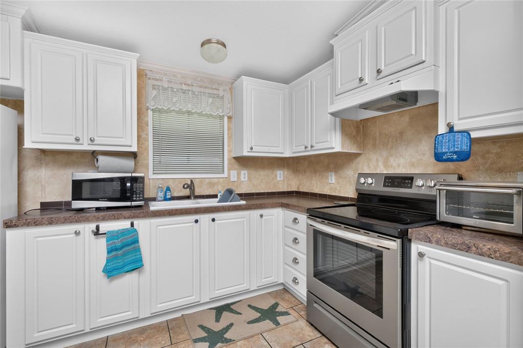 A kitchen features white cabinets, dark laminate countertops, stainless steel appliances, and tiled flooring — 7464 DANVERS CIRCLE, PORT CHARLOTTE, FL