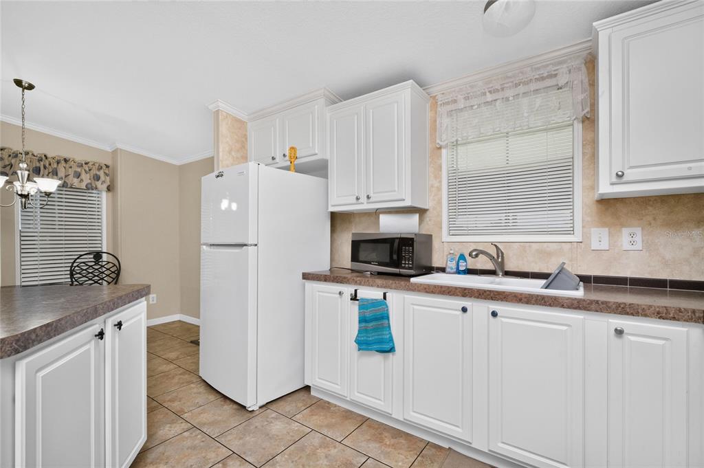 A kitchen features white cabinetry, a white refrigerator, a microwave, and brown laminate countertops — 7464 DANVERS CIRCLE, PORT CHARLOTTE, FL