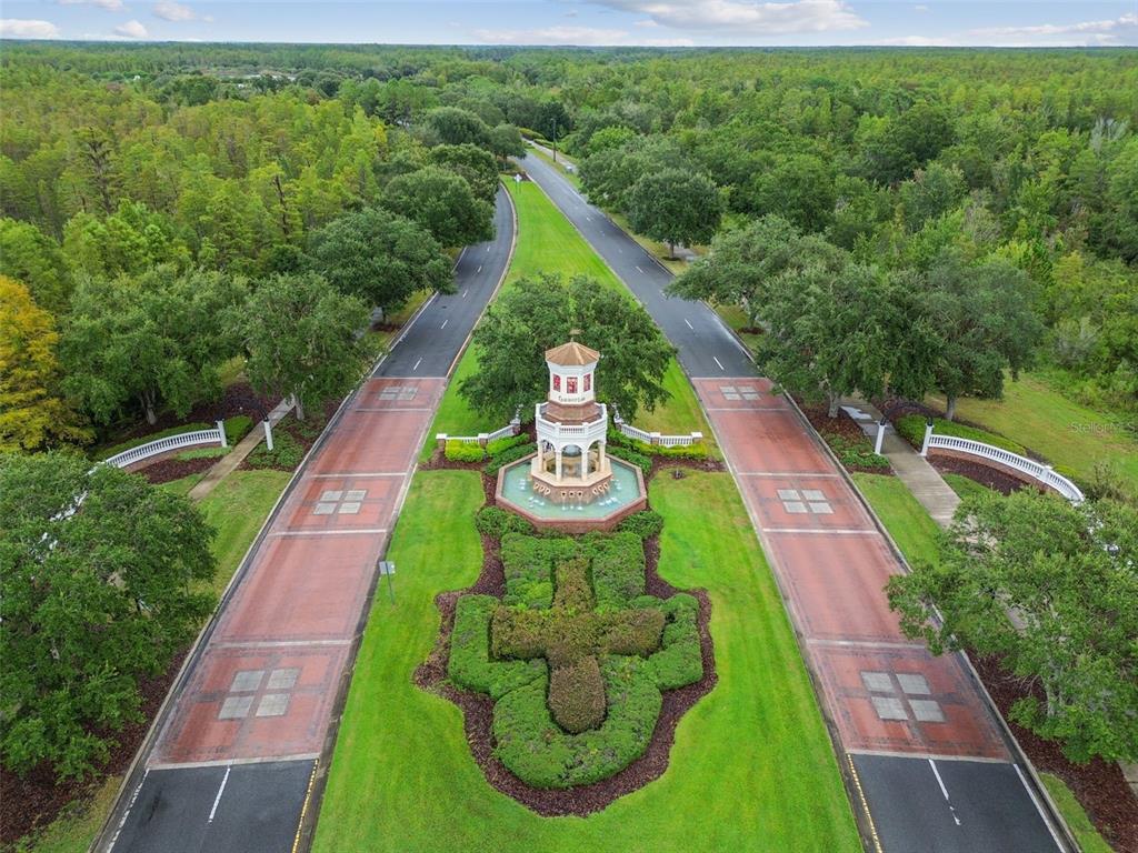An aerial view shows a gated community entrance with a central fountain and clock tower — 8318 SWISS CHARD CIRCLE, LAND O LAKES, FL