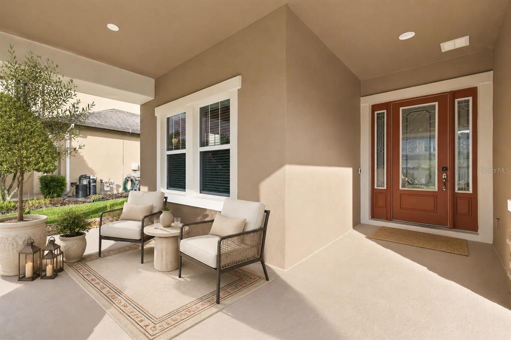 A covered front porch features two chairs, a small table, and a decorative front door — 8318 SWISS CHARD CIRCLE, LAND O LAKES, FL