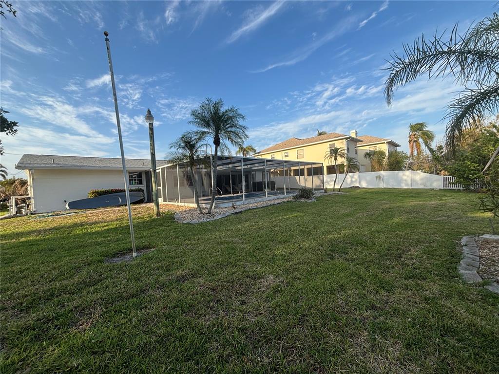 A backyard view showing a house with a screened-in pool enclosure and a grassy lawn — 4411 DOLPHIN LANE, PALMETTO, FL