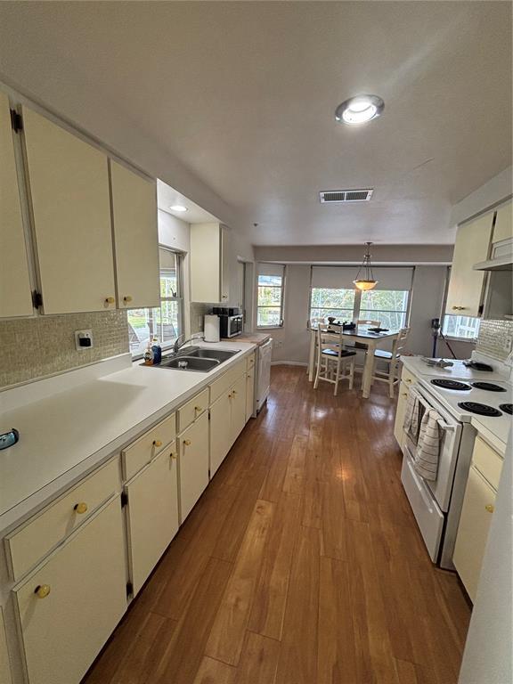A kitchen with light-colored cabinets, white countertops, and wood-look flooring leads into a dining area — 4411 DOLPHIN LANE, PALMETTO, FL