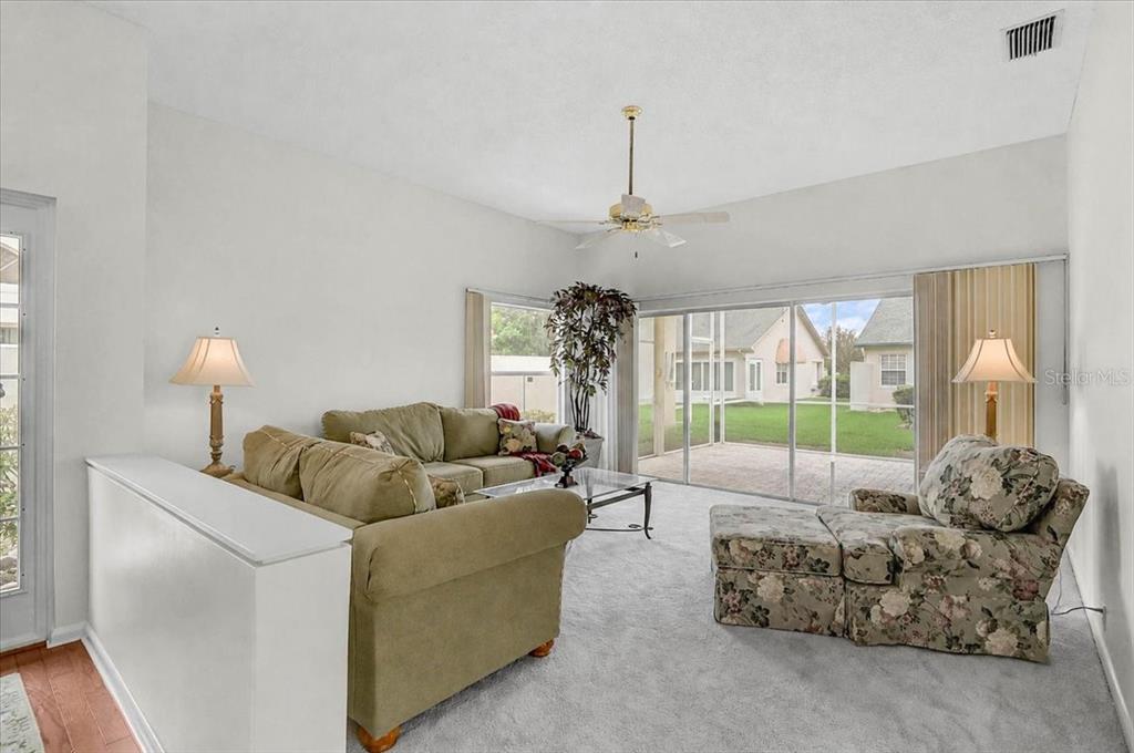 A living room with a half-wall, beige carpet, and a sliding glass door to a patio — 4717 PERIDIA BOULEVARD E, BRADENTON, FL
