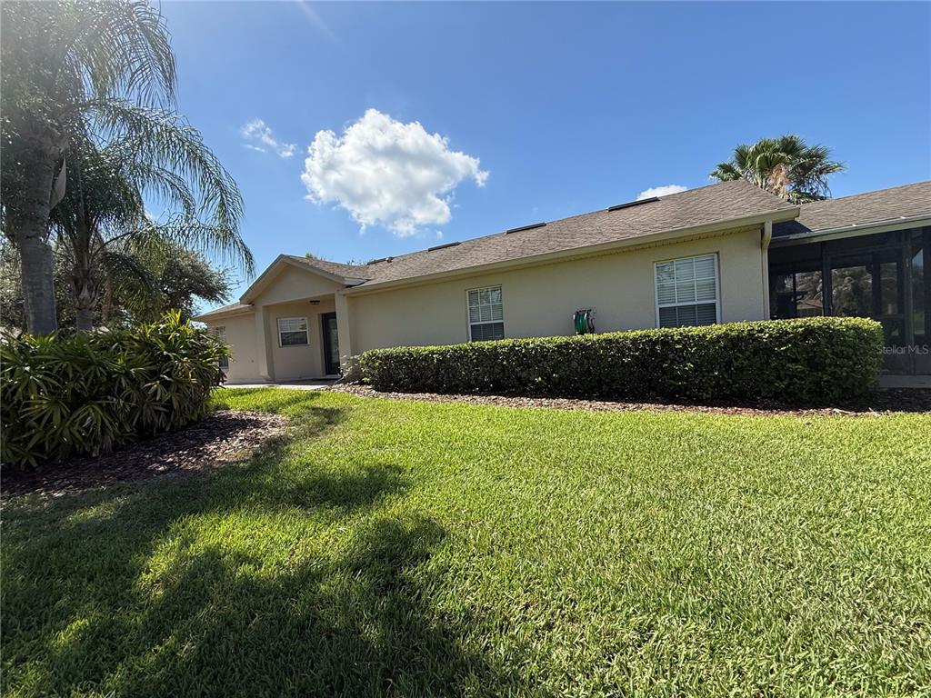 A view of a house exterior with a green lawn, hedge, and screened-in patio — 674 VINEYARD WAY, POINCIANA, FL